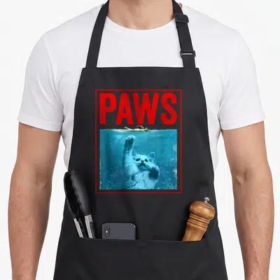 Tablier de cuisine noir avec illustration parodiant un film d'action montrant un chat géant sous l'eau et le mot Paws en rouge.