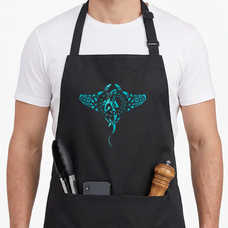 Tablier de cuisine noir avec une raie manta tribale turquoise stylisée au centre du torse.