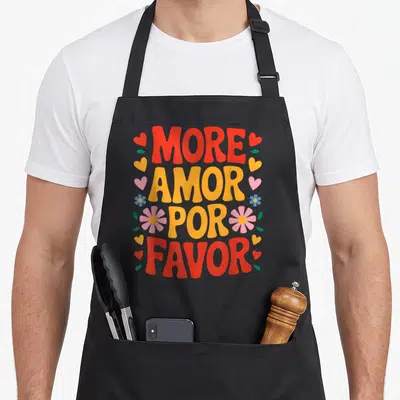 Tablier de cuisine noir avec inscription More Amor Por Favor entourée de cœurs et de fleurs colorées.