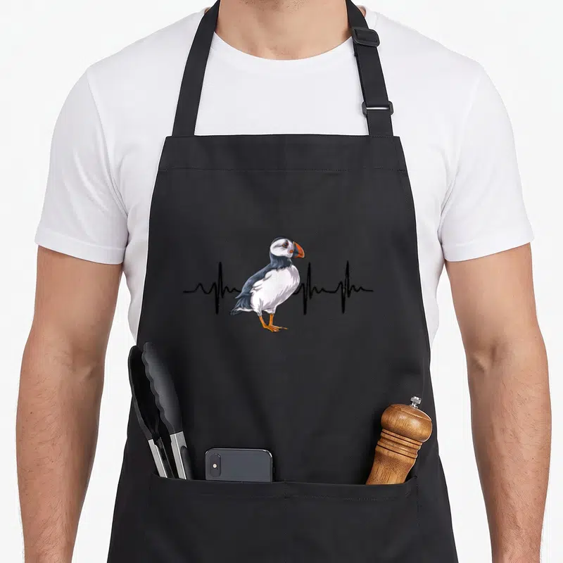 Tablier de cuisine noir avec illustration de pingouin et ligne de rythme cardiaque noire.