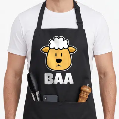 Tablier de cuisine noir avec tête de mouton jaune et blanc et le texte BAA en grosses lettres blanches.