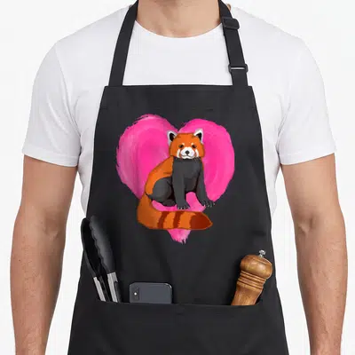 Tablier de cuisine noir avec illustration d'un panda roux assis devant un cœur rose vif.