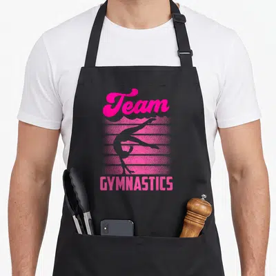 Tablier de cuisine noir avec l'inscription Team Gymnastics et une silhouette de gymnaste en rose vif sur fond strié.