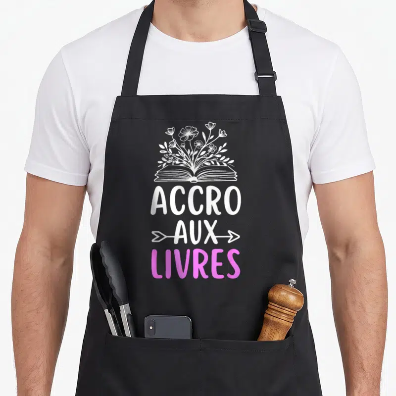 Tablier de cuisine noir avec illustration d'un livre ouvert fleurissant et texte accro aux livres en blanc et rose.