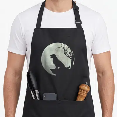 Tablier de cuisine noir avec silhouette chien assis face à une grande lune pleine et un arbre sec.
