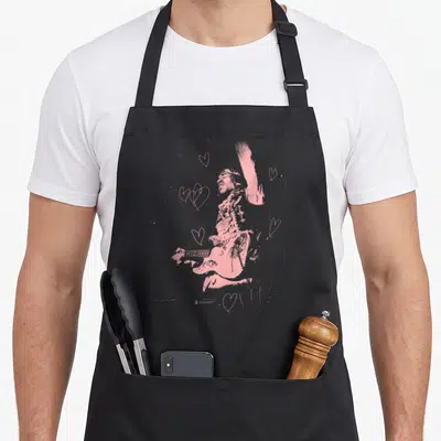 Tablier de cuisine noir avec portrait rose de Jimi Hendrix jouant de la guitare entouré de cœurs stylisés.