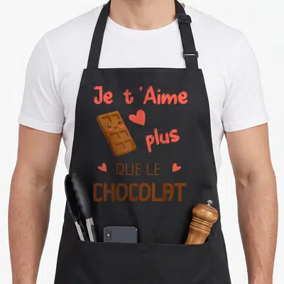 Tablier de cuisine noir avec une illustration de chocolat souriant et le texte Je t'Aime plus que le chocolat en rose et brun.