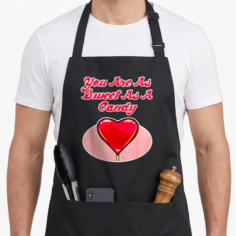 Tablier de cuisine noir avec un cœur rouge lollipop et le texte You Are As Sweet As A Candy en lettres roses.