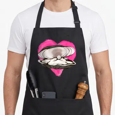 Tablier de cuisine noir avec illustration d'une huître ouverte sur un cœur rose vif contenant une perle blanche.