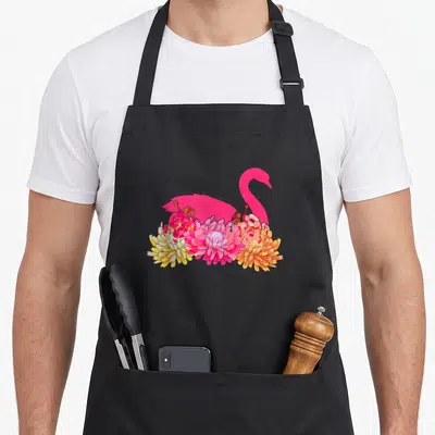 Tablier de cuisine noir avec un cygne rose stylisé entouré de fleurs colorées.
