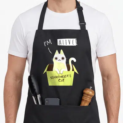 Tablier de cuisine noir avec un chat blanc dans une boîte jaune portant l'inscription SCHRÖDINGER'S CAT.
