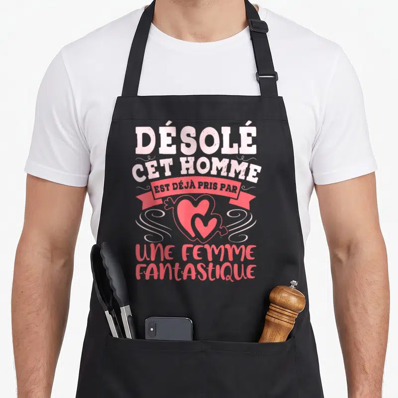 Tablier de cuisine noir avec inscription rose « Désolé cet homme est déjà pris par une femme fantastique » et deux cœurs superposés.