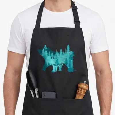 Tablier de cuisine noir avec silhouette d'ours grizzly remplie d'une forêt d'épinettes turquoise et bleu canard.