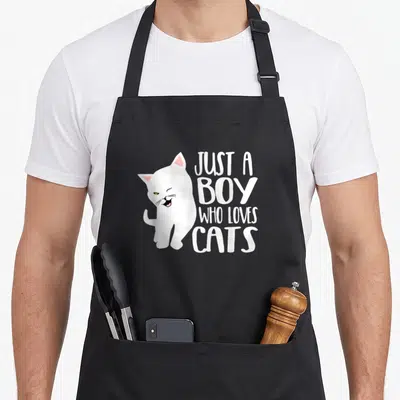 Tablier de cuisine noir avec illustration d'un chat blanc et du texte Juste un garçon qui aime les cats en blanc.