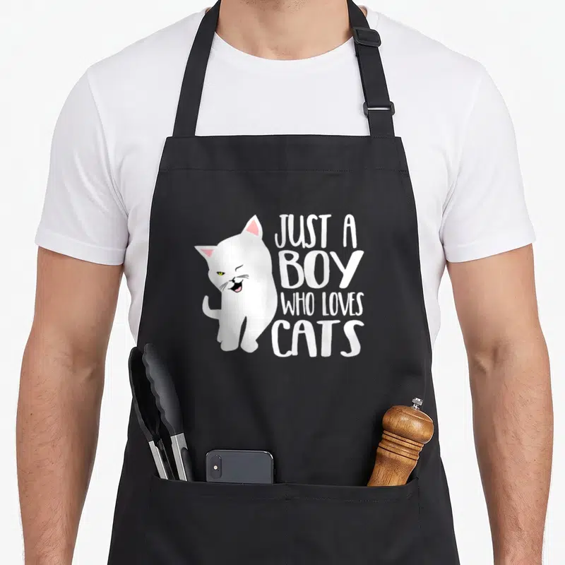 Tablier de cuisine noir avec illustration d'un chat blanc et du texte Juste un garçon qui aime les cats en blanc.