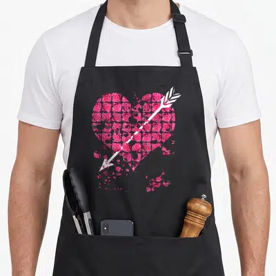 Tablier de cuisine noir avec un grand coeur rose composé de roses et d'une flèche blanche traversante.