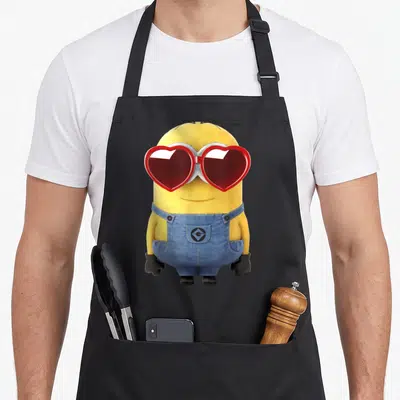 Tablier de cuisine noir avec un minion jaune portant des lunettes rouge en forme de cœur et une salopette bleue.