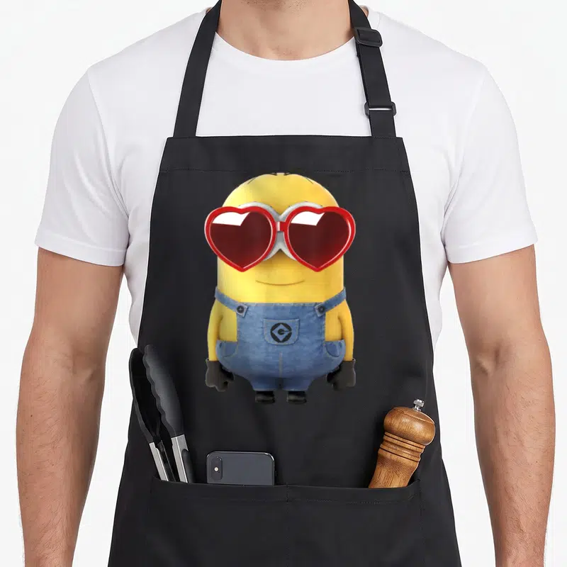 Tablier de cuisine noir avec un minion jaune portant des lunettes rouge en forme de cœur et une salopette bleue.
