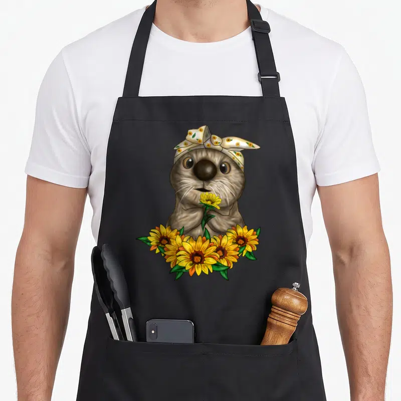 Tablier de cuisine noir avec une loutre mignonne portant un foulard à fleurs et tenant un bouquet de tournesols jaunes.