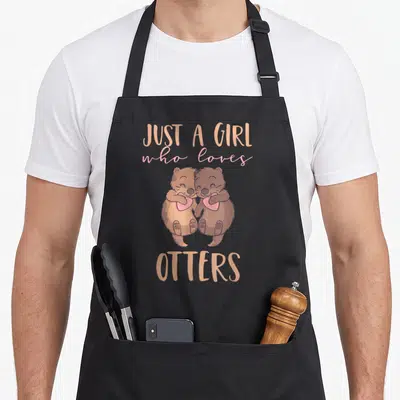 Tablier de cuisine noir avec deux loutres s'embrassant tenant des cœurs roses et texte en anglais.