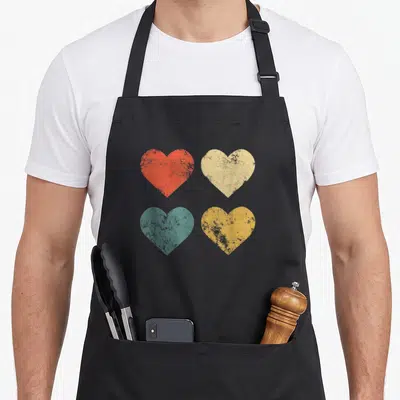 Tablier de cuisine noir avec quatre coeurs vintage rouge, beige, turquoise et jaune disposés en grille.