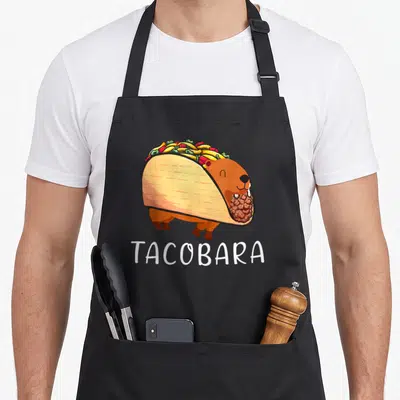 Tablier de cuisine noir avec illustration d'une capybara en forme de taco et le mot Tacobara en blanc.