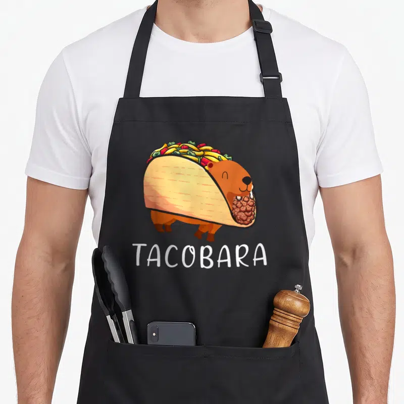 Tablier de cuisine noir avec illustration d'une capybara en forme de taco et le mot Tacobara en blanc.
