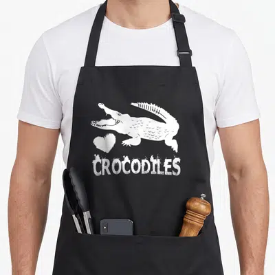 Tablier de cuisine noir avec illustration blanche d'un crocodile, un cœur et le mot CROCODILES en bas.