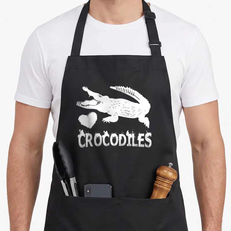 Tablier de cuisine noir avec illustration blanche d'un crocodile, un cœur et le mot CROCODILES en bas.