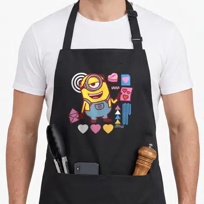 Tablier de cuisine noir avec un Minion jaune tenant une carte aux cœurs et des éléments de Saint-Valentin colorés.