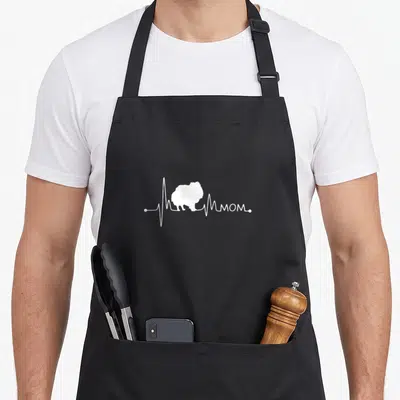 Tablier de cuisine noir avec silhouette blanche de chien Poméranie et inscription Mom sur fond gris uni.