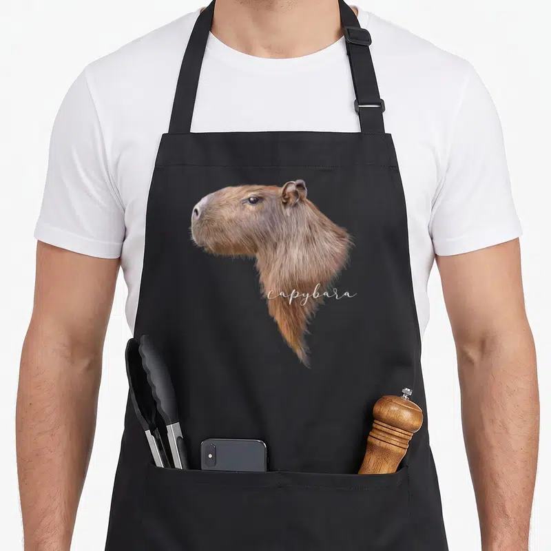 Tablier de cuisine noir avec portrait réaliste de capybara et texte capybara en blanc
