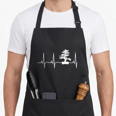 Tablier de cuisine noir avec un motif blanc représentant un bonsai au centre d'une ligne de rythme cardiaque.