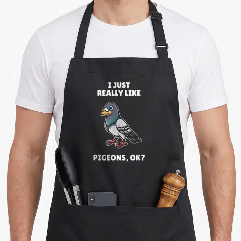 Tablier de cuisine noir avec illustration d'un pigeon aux yeux bleus et le texte I Just Really Like Pigeons OK imprimé en blanc.