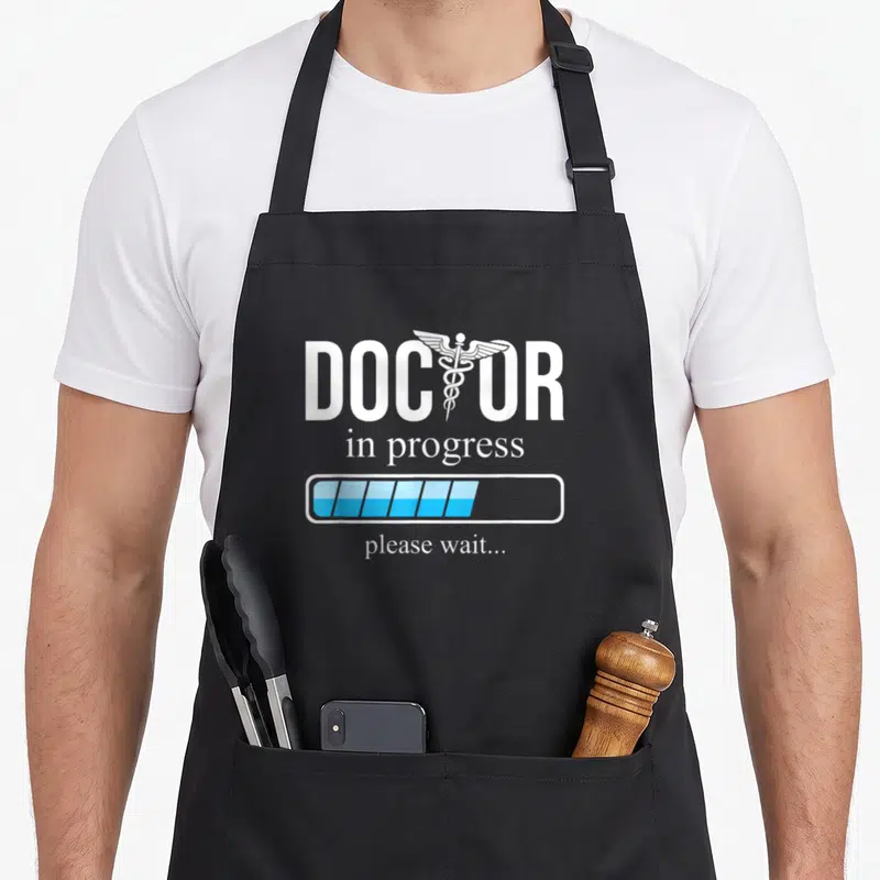 Tablier de cuisine noir avec inscription Doctor in progress et barre de chargement bleue.