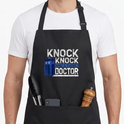 Tablier de cuisine noir avec une cabine téléphonique bleue et le texte blanc « Knock knock who's there docteur » en typographie usée.