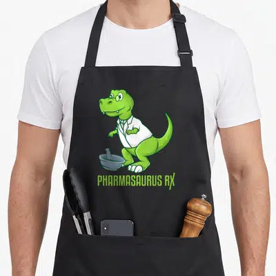 Tablier de cuisine noir avec un dinosaure pharmacien vert portant une blouse blanche et tenant un pilon à côté du texte Pharmasaurus RX.