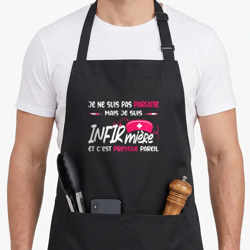 Tablier de cuisine noir avec inscription Je ne suis pas parfaite mais je suis infirmière et casque rose à croix blanche.