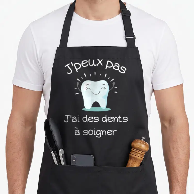 Tablier de cuisine noir avec une illustration de dent bleue souriante et le texte J'peux pas j'ai des dents à soigner en blanc.