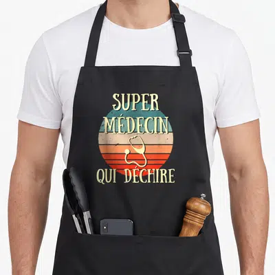 Tablier de cuisine noir avec un soleil rétro orange et bleu, un stéthoscope jaune et le texte super médecin qui déchire en lettres capitales.