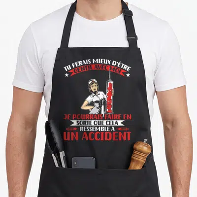 Tablier de cuisine noir avec infirmière tenant une grande seringue rouge et texte humoristique en blanc et rouge.