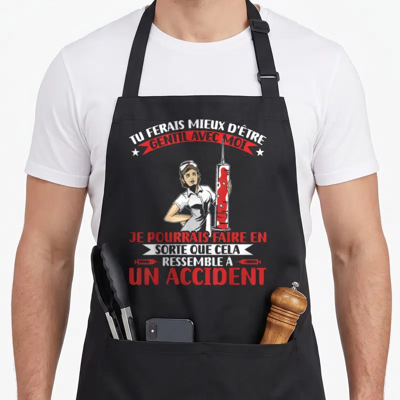Tablier de cuisine noir avec infirmière tenant une grande seringue rouge et texte humoristique en blanc et rouge.
