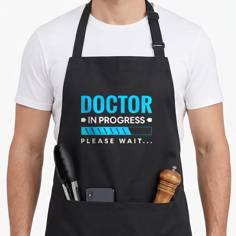 Tablier de cuisine noir avec inscription DOCTOR IN PROGRESS et graphique de chargement bleu et blanc.