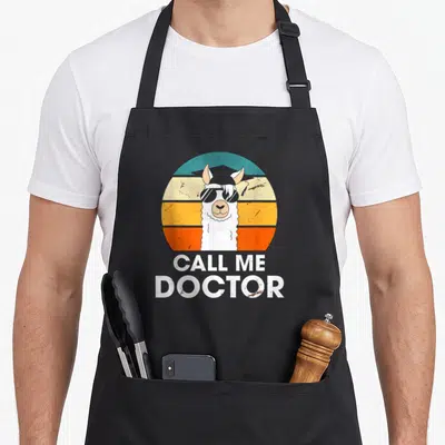 Tablier de cuisine noir avec illustration d'un lama portant des lunettes de soleil et un stéthoscope sur fond circulaire multicolore.