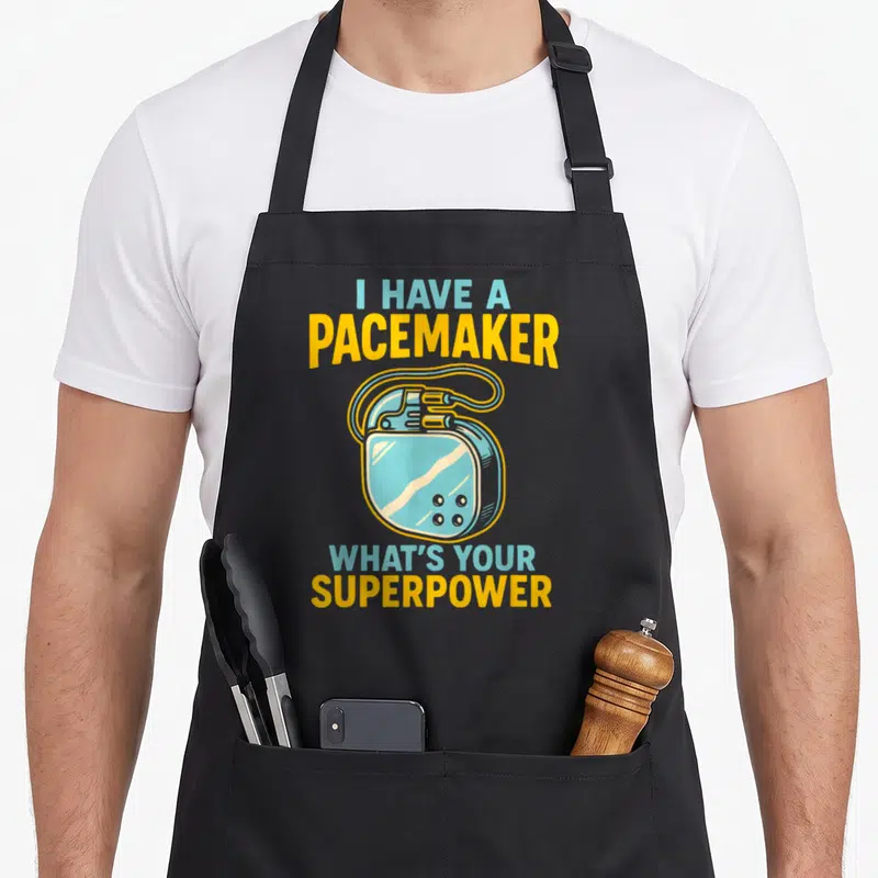 Tablier de cuisine noir avec illustration d'un pacemaker bleu et texte jaune et turquoise sur fond uni.