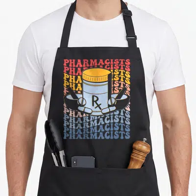 Tablier de cuisine noir avec illustration d'un flacon Rx, pilules et mortiers sur fond de texte répété coloré.