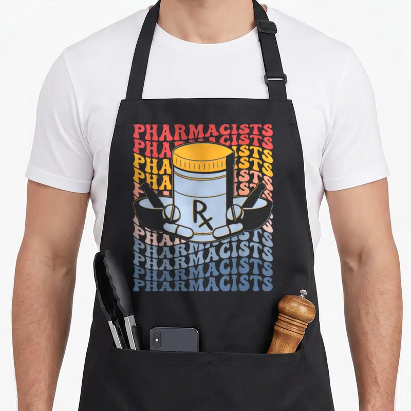 Tablier de cuisine noir avec illustration d'un flacon Rx, pilules et mortiers sur fond de texte répété coloré.