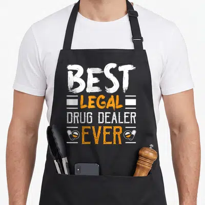 Tablier de cuisine noir avec inscription Best Legal Drug Dealer Ever et deux capsules oranges.