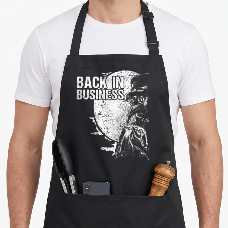 Tablier de cuisine noir avec illustration blanche d'un médecin de la peste et texte Back in Business.