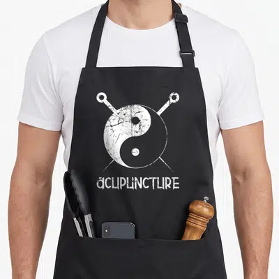 Tablier de cuisine noir avec symbole Yin Yang blanc traversé par deux aiguilles d'acupuncture et le mot Acupuncture en bas.